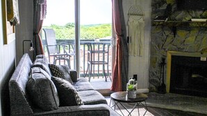Una sala de estar con un sofá gris, una mesita redonda y una cesta de mimbre. Hay un balcón con una silla y una mesa afuera.