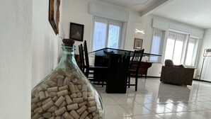 Une pièce spacieuse comprenant un coin repas, un grand vase en verre rempli de bouchons et une fenêtre avec des rideaux.