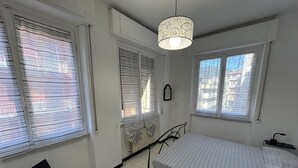 Une chambre à coucher avec un lit, une chaise, un luminaire suspendu et des fenêtres équipées de stores.