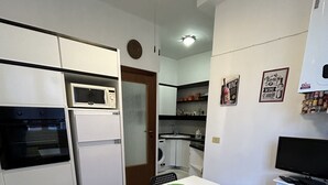 Une cuisine de taille réduite avec une table blanche, un saladier vert et deux chaises.