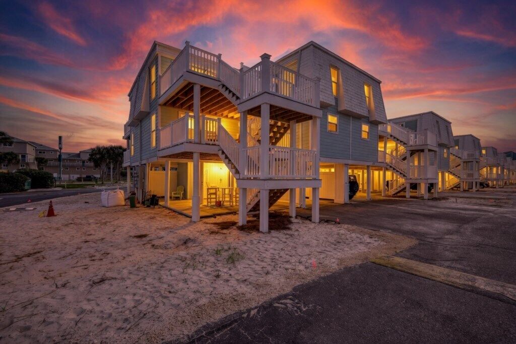 A beachfront property with multiple levels, outdoor seating, and a staircase leading to the entrance.