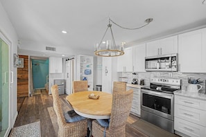 A modern kitchen with white cabinetry, a stainless steel oven, and a dining area with wicker chairs.