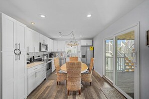 A modern kitchen with white cabinetry, a dining table with wicker chairs, and a chandelier.