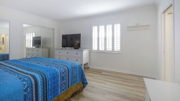 A bedroom with a bed, a dresser, a television, and a window with blinds. - Luxury Gulf-Front Condo w/ Balcony Views | 3BR/2BA | Pool | Beach Access | Sleeps 6 | Great Sunsets | Anna Maria Island (Holmes Beach)