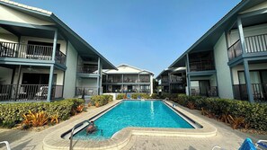 A hotel with a central swimming pool, multiple balconies, and a clear sky.
