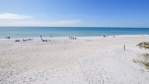 A wide sandy beach with footprints, a few people, and a clear blue sky. - Luxury Gulf-Front Condo w/ Balcony Views | 3BR/2BA | Pool | Beach Access | Sleeps 6 | Great Sunsets | Anna Maria Island (Holmes Beach)