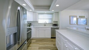 A modern kitchen with white cabinetry, stainless steel appliances, and a wooden floor. - Luxury Gulf-Front Condo w/ Balcony Views | 3BR/2BA | Pool | Beach Access | Sleeps 6 | Great Sunsets | Anna Maria Island (Holmes Beach)