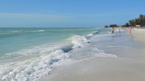 A beach with clear turquoise water, gentle waves, and people walking along the shore. - Luxury Gulf-Front Condo w/ Balcony Views | 3BR/2BA | Pool | Beach Access | Sleeps 6 | Great Sunsets | Anna Maria Island (Holmes Beach)