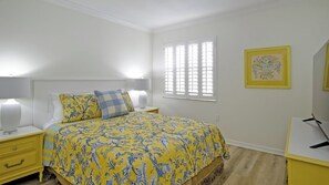 A bedroom with a bed, bedside tables, a lamp, a window with blinds, and a framed picture on the wall. - Luxury Gulf-Front Condo w/ Balcony Views | 3BR/2BA | Pool | Beach Access | Sleeps 6 | Great Sunsets | Anna Maria Island (Holmes Beach)