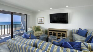 A living room with a view of the ocean, a large flat-screen TV, and striped sofas. - Luxury Gulf-Front Condo w/ Balcony Views | 3BR/2BA | Pool | Beach Access | Sleeps 6 | Great Sunsets | Anna Maria Island (Holmes Beach)
