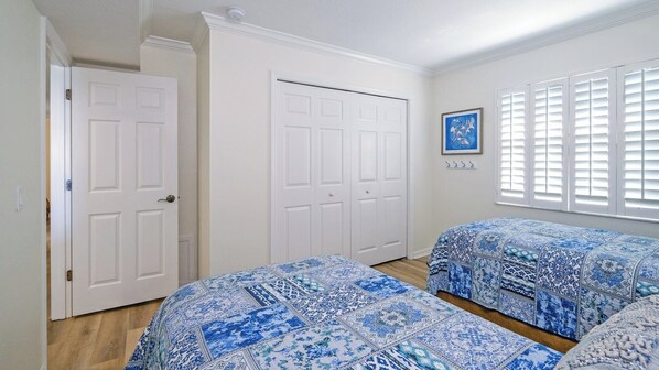 A bedroom with two beds, white doors, a window with blinds, and a framed picture on the wall.