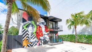A modern building with a colorful mural on the side, a balcony, and palm trees in the background. - Wynwood Charm 1, Live the art.1 Free Gated Parking (Miami)