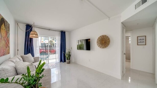 A spacious living area with a sofa, a TV, and a large window with curtains. - Wynwood Charm 1, Live the art.1 Free Gated Parking (Miami)