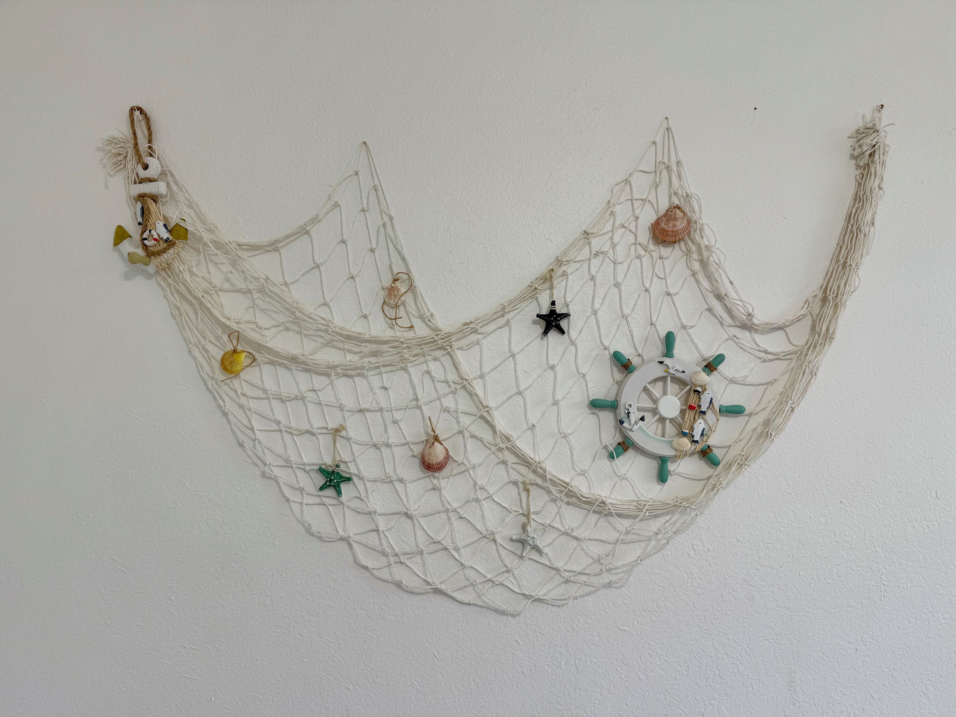 A decorative wall hanging with a net-like structure, featuring seashells and a ship's wheel ornament.