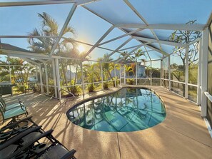 A covered outdoor swimming pool with a glass ceiling, surrounded by palm trees and a view of a residential area. - Ellie’s Landing 3 – Cozy Lanai Retreat w/ Heated Pool (Port Charlotte)