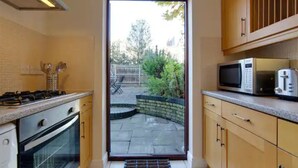 A kitchen with a stove, oven, microwave, and cabinets. There is a door leading to a patio with a brick wall and greenery. - Pass the Keys | Modern and Spacious Terrace in Central Cambridge (Cambridge)