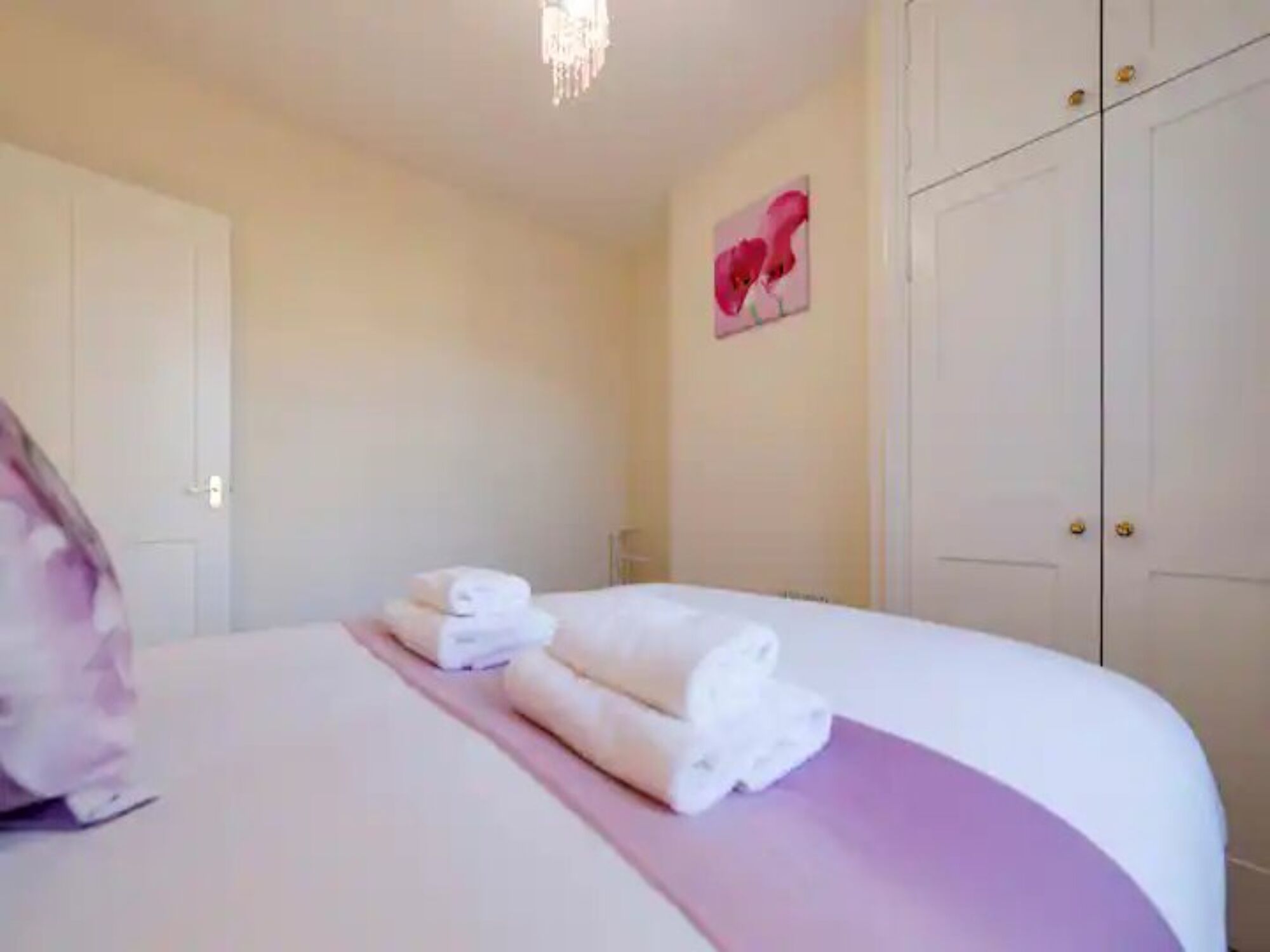 A hotel room with a bed, a pink accent wall, a door, and a wall decoration.