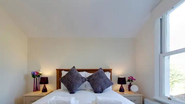 A neatly made bed with two pillows, two bedside tables with lamps, and a window with a view. - Pass the Keys | Modern and Spacious Terrace in Central Cambridge (Cambridge)