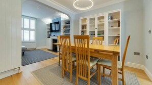 Un comedor con una mesa y sillas de madera, rodeado de estanterías blancas con libros y objetos decorativos.