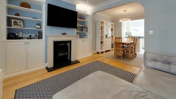Una sala de estar moderna con chimenea, estanterías empotradas, un televisor de pantalla plana y un comedor con mesa y sillas.