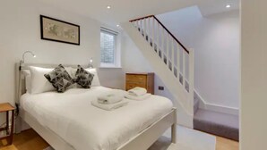 Un dormitorio moderno con una cama grande, una mesita de noche de madera, un cuadro enmarcado en la pared y una escalera que conduce a un nivel superior.