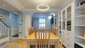 Un comedor con una mesa y sillas de madera, un armario blanco con puertas de cristal y un tapete estampado en el suelo.