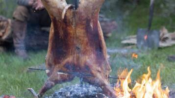 A roasted animal over an open fire with a man in the background.