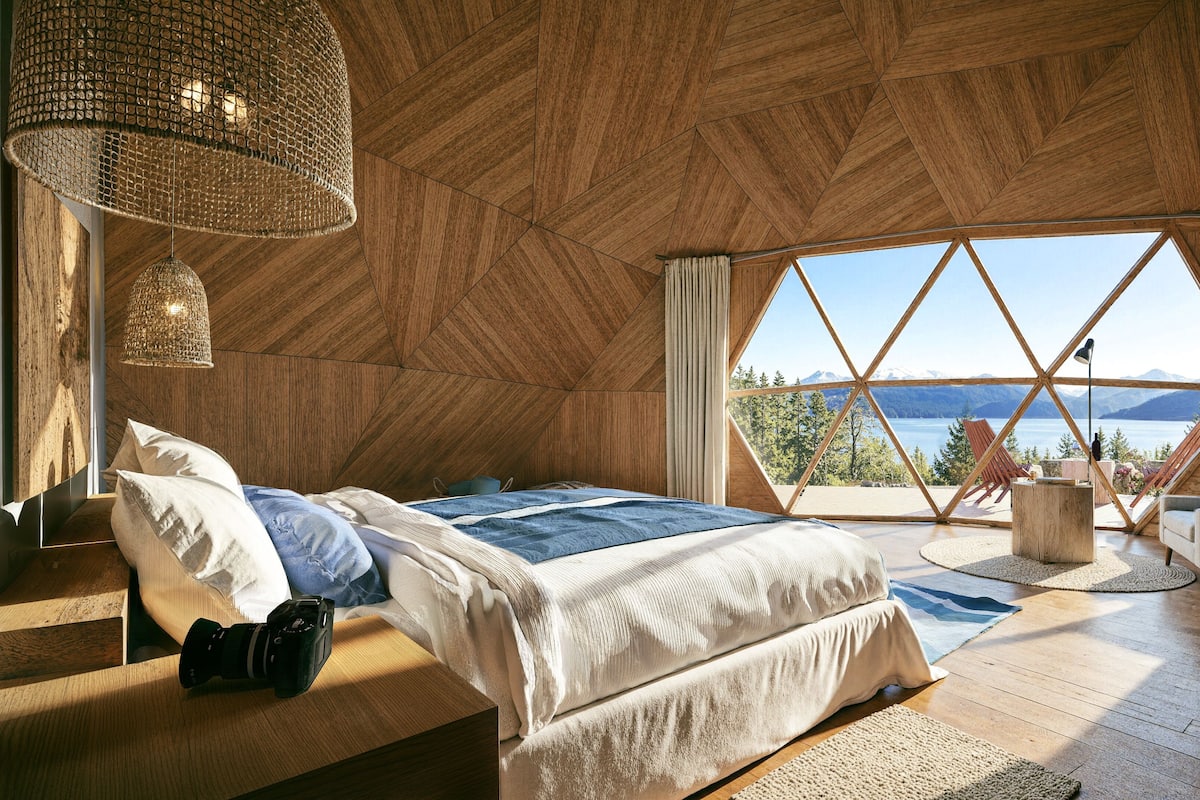 A bedroom with a large bed, a wooden ceiling, a view of the outdoors, and a window with curtains.