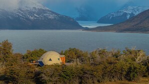 A dome-shaped building near a body of water with mountains in the background.