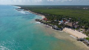 An aerial view of a coastal area with a beach, houses, and a clear sky. - Tropicalito Tulum (Tulum)