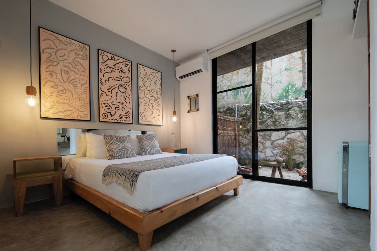 Un dormitorio con una cama de madera, una mesita de noche y un gran ventanal con vistas a un jardín.