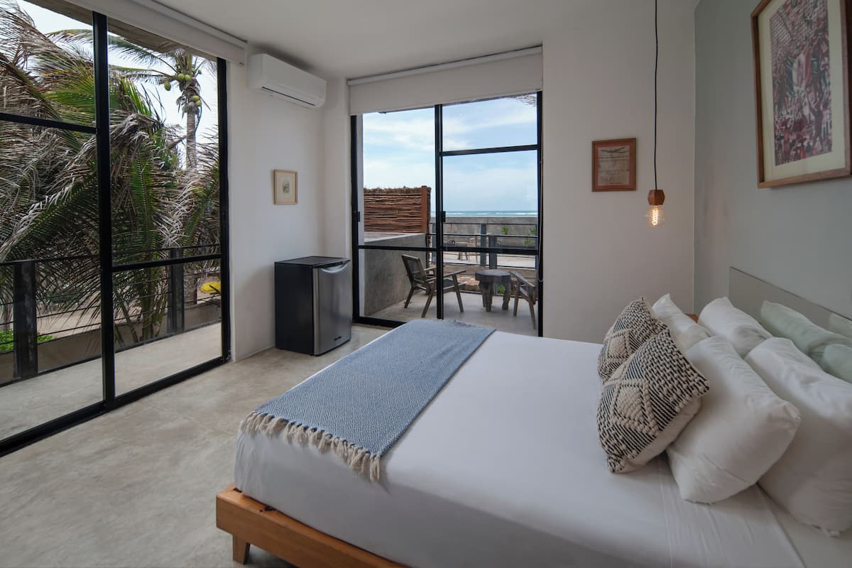 Un dormitorio con una cama grande, un balcón con vista al océano y una pequeña zona de estar con una mesa y sillas.