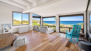 Una habitación amplia con un gran ventanal con vistas al océano, una zona de estar acogedora y una chimenea.