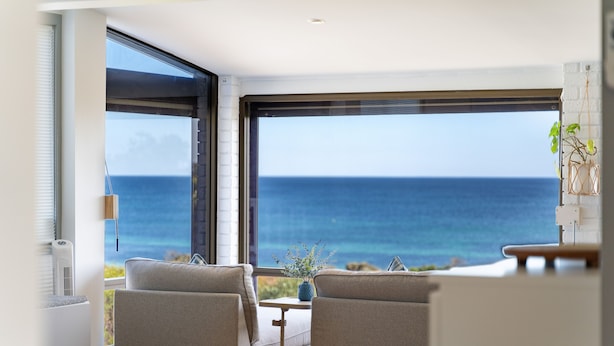 A modern living room with a large window overlooking the ocean, a comfortable sofa, and a small table with a vase.