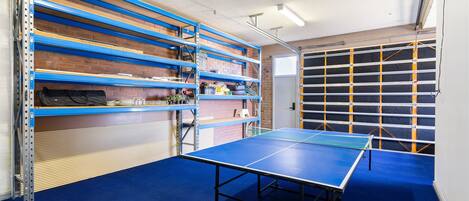A room with a ping pong table, shelving units, and a garage door.