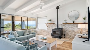 A modern living room with a fireplace, a sofa set, a coffee table, and a large window offering a view of the outdoors.