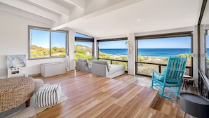 A spacious room with a large window overlooking the ocean, a cozy seating area, and a fireplace.
