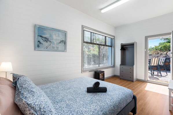 A bedroom with a bed, a nightstand, a dresser, a window with blinds, and a door leading to an outdoor area.
