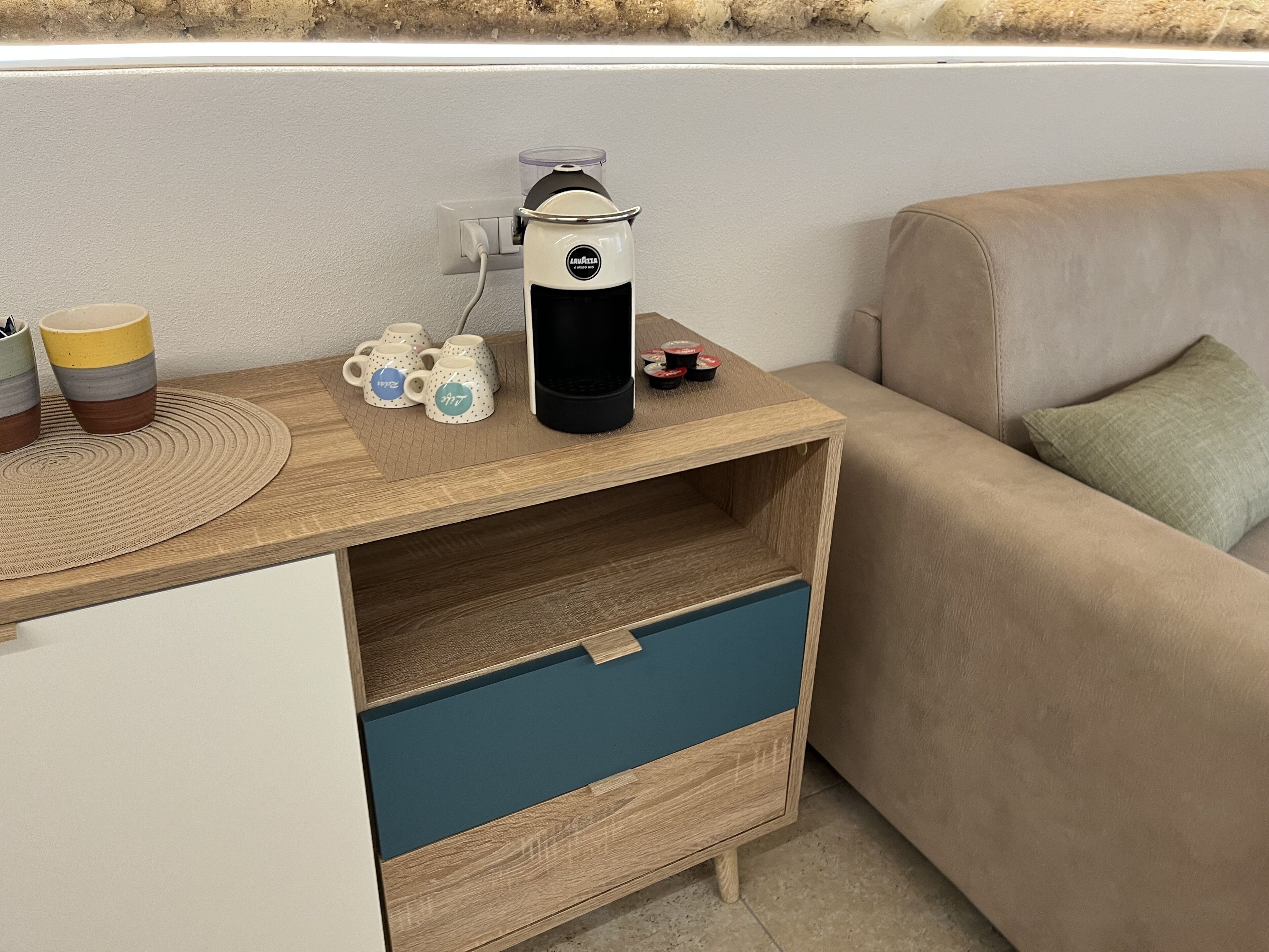 Una pequeña kitchenette con cafetera, tazas y tetera sobre una encimera de madera.