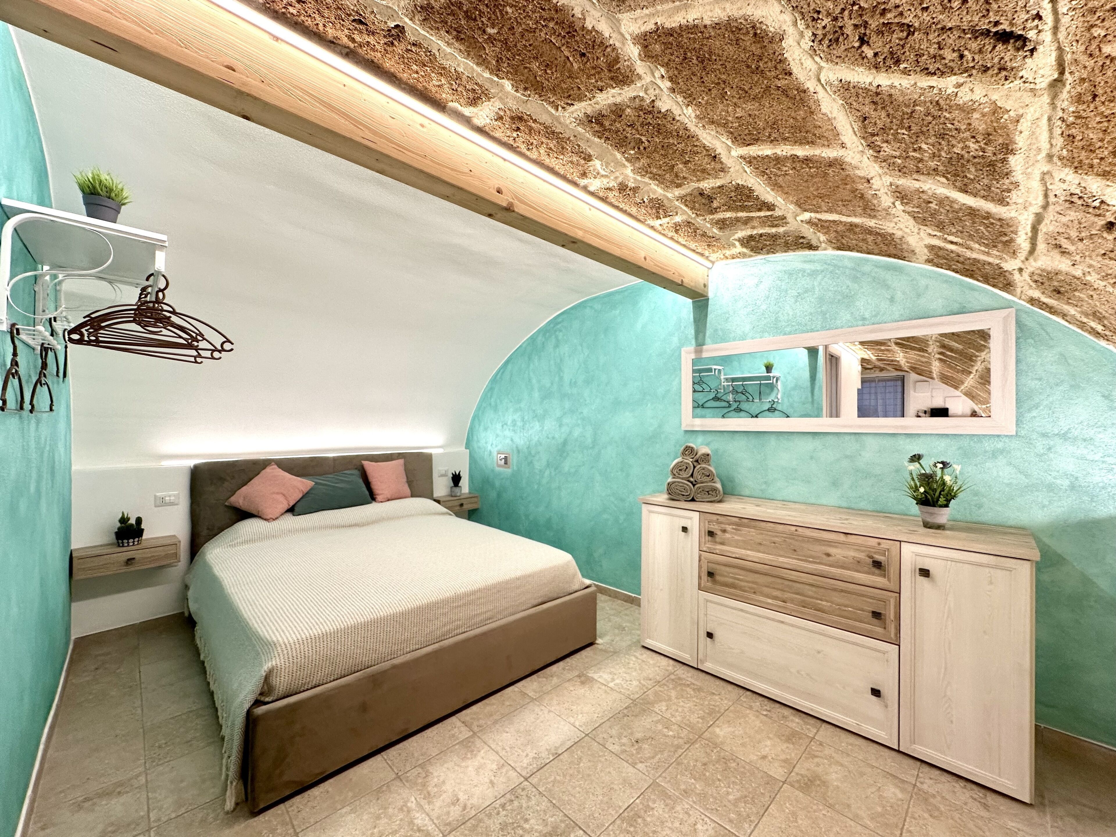 Une chambre avec un plafond en pierre, un lit avec une tête de lit, une table de chevet, une commode et un miroir.