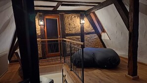 Camera mansardata con travi a vista in legno, parete in pietra, scala in legno e un sacco di fagioli nero.