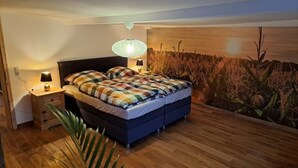Una camera da letto con un letto, lampade da comodino, un comodino, pavimento in legno e un affresco sulla parete.