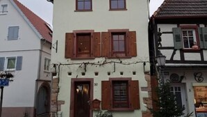 Un edificio a due piani con un tetto spiovente, un ingresso centrale con una porta in legno e un piccolo portico.