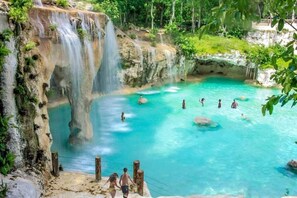 A natural pool with clear turquoise water, surrounded by rocky cliffs and lush greenery.