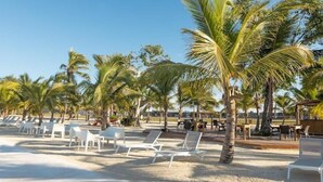 Een strand met witte ligbedden en palmbomen.
