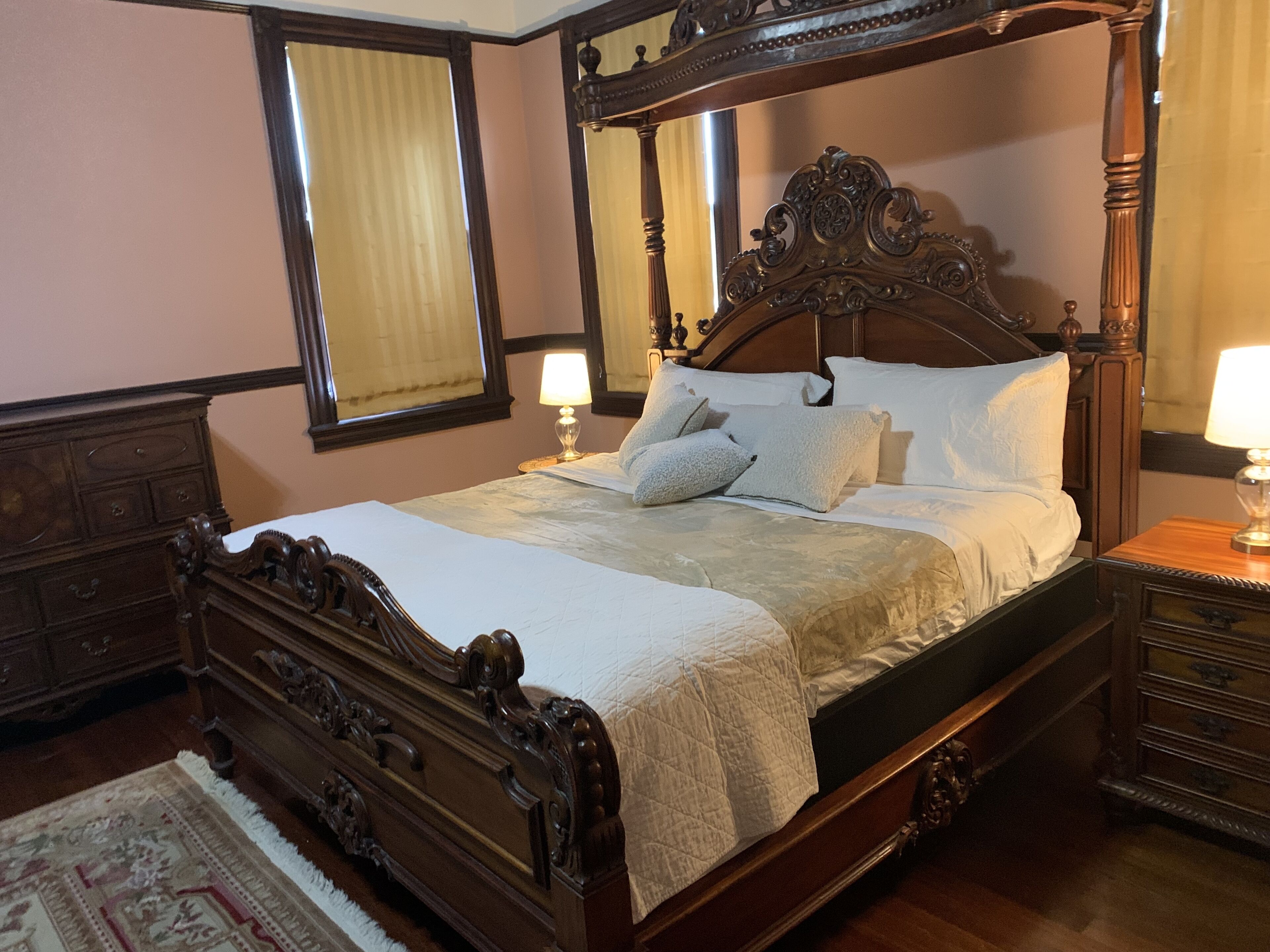Un letto a baldacchino tradizionale con struttura in legno e decorazioni elaborate, affiancato da comodini e una cassettiera coordinati.