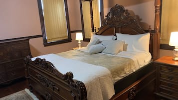 A traditional four-poster bed with a wooden frame and ornate carvings, accompanied by matching nightstands and a dresser.