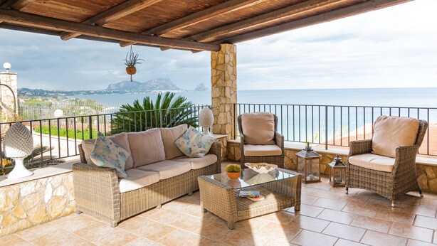 A covered outdoor seating area with wicker furniture, a stone pillar, and a view of the sea. - Gorgeous Villa with outbuilding for a relaxing vacation (Torre Colonna-Sperone)