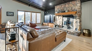 A spacious living room with a stone fireplace, leather sofa, and a large window offering a view of the outdoors. - Lake Arbutus Retreat w/ Hot Tub & Game Room (Neillsville)