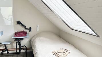 Et lille værelse med en enkeltseng, skråvæg, skrivebord med stol og en radiator.